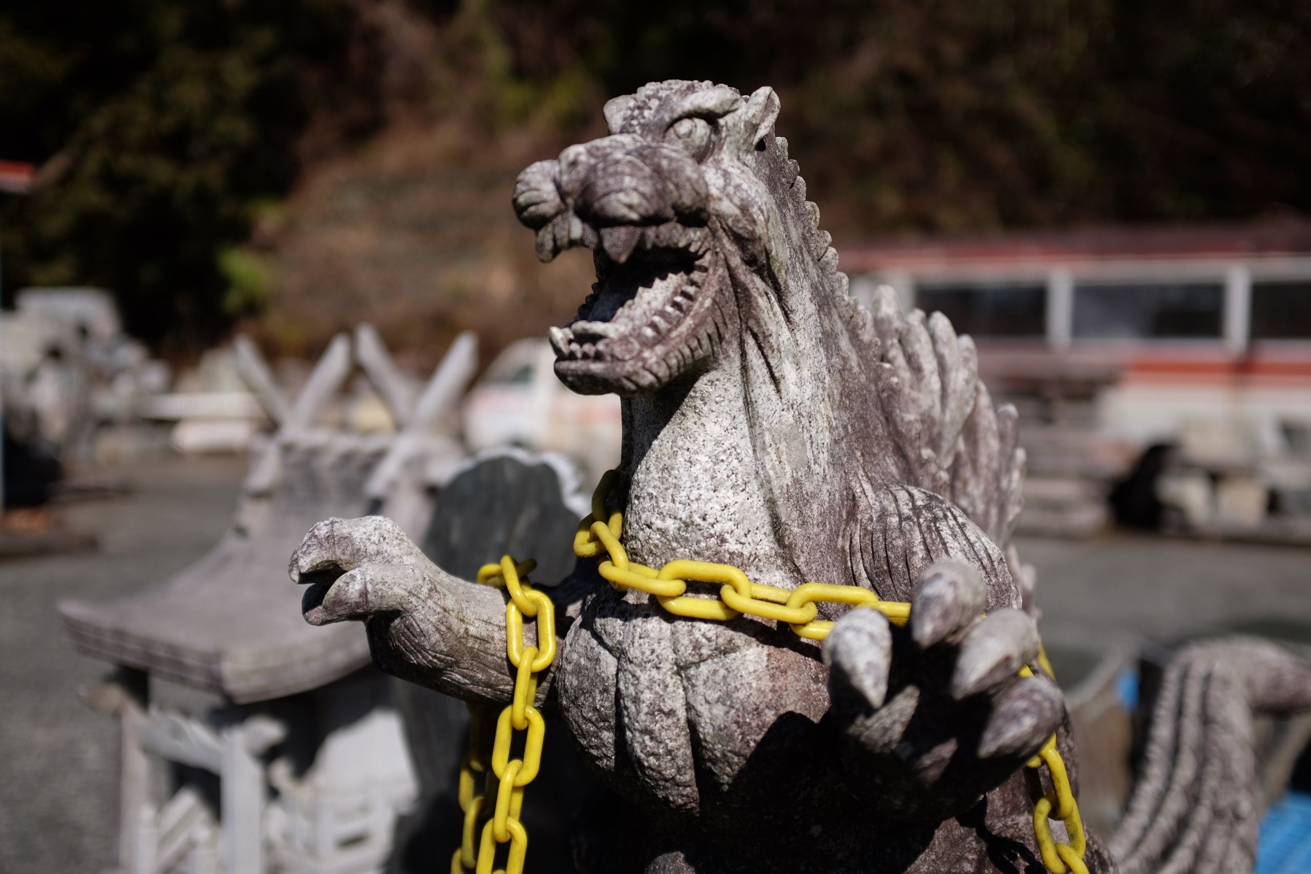 A stone Godzilla statue tied down with a yellow chain.
