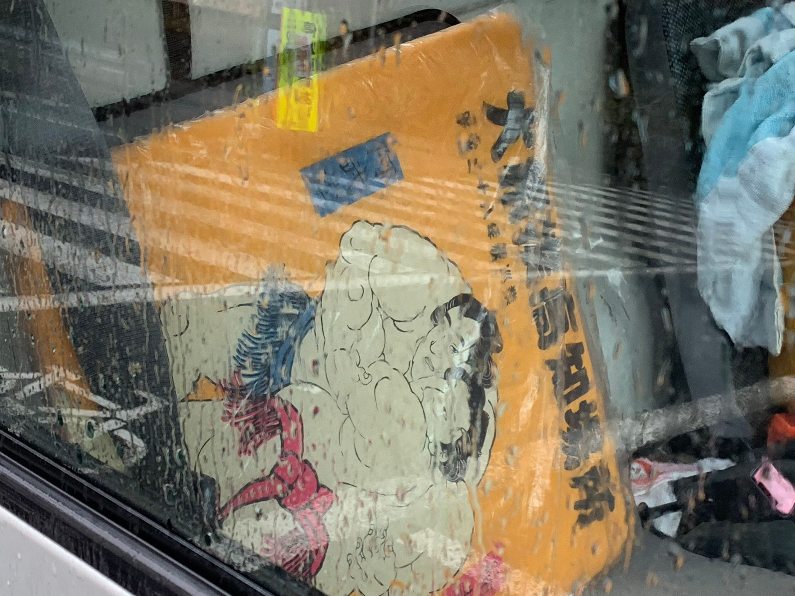Looking through the wet window of another car, a picture of two medieval sumo wrestlers in the driver’s seat.
