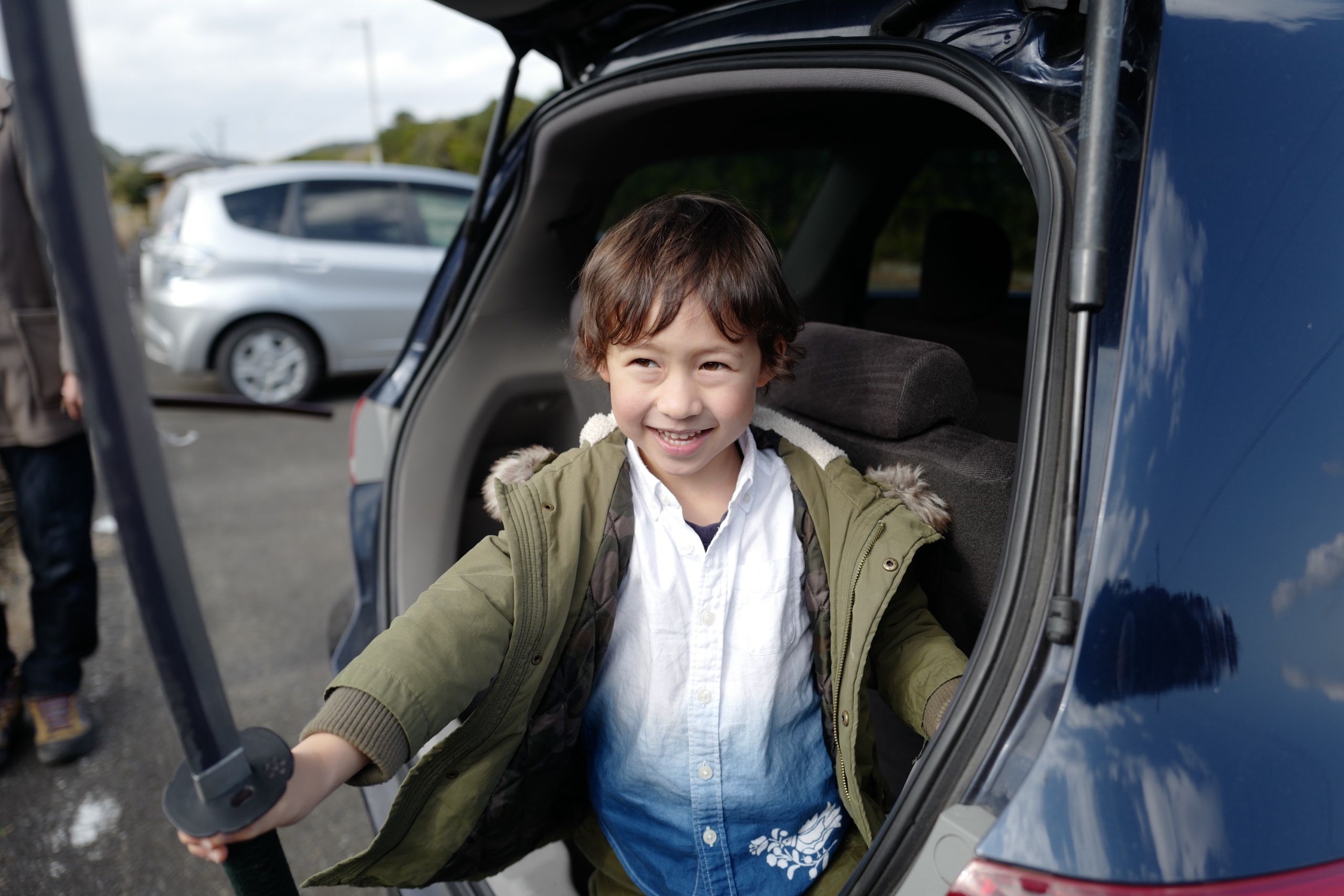 A young boy in a green parka and a hand-dyed indigo shirt, Hanga’s son Mihály, brandises a samurai sword as he stands in the trunk of a car.