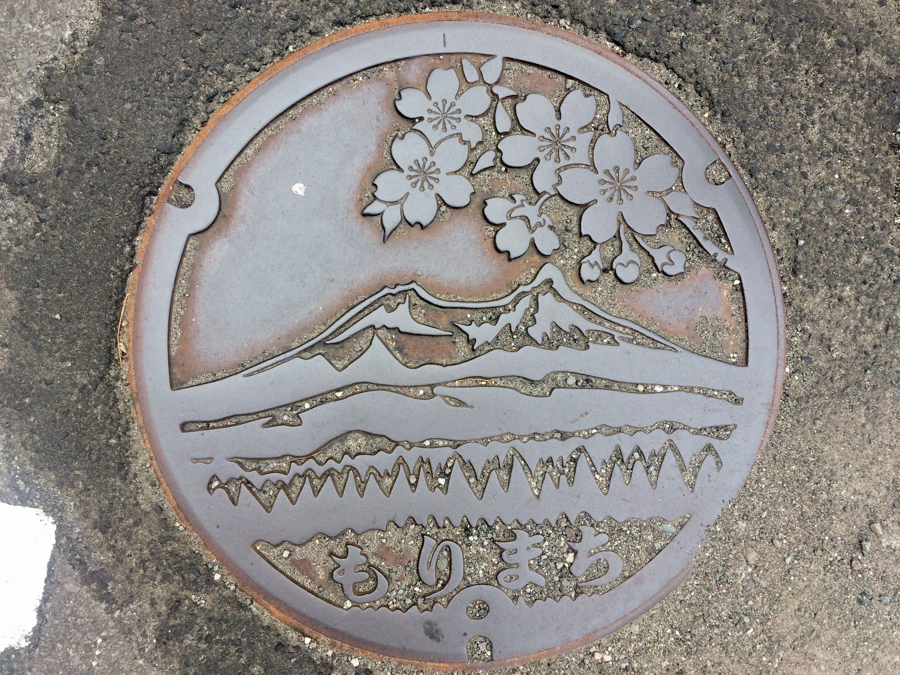 A manhole cover shows Mount Komagatake from another angle.