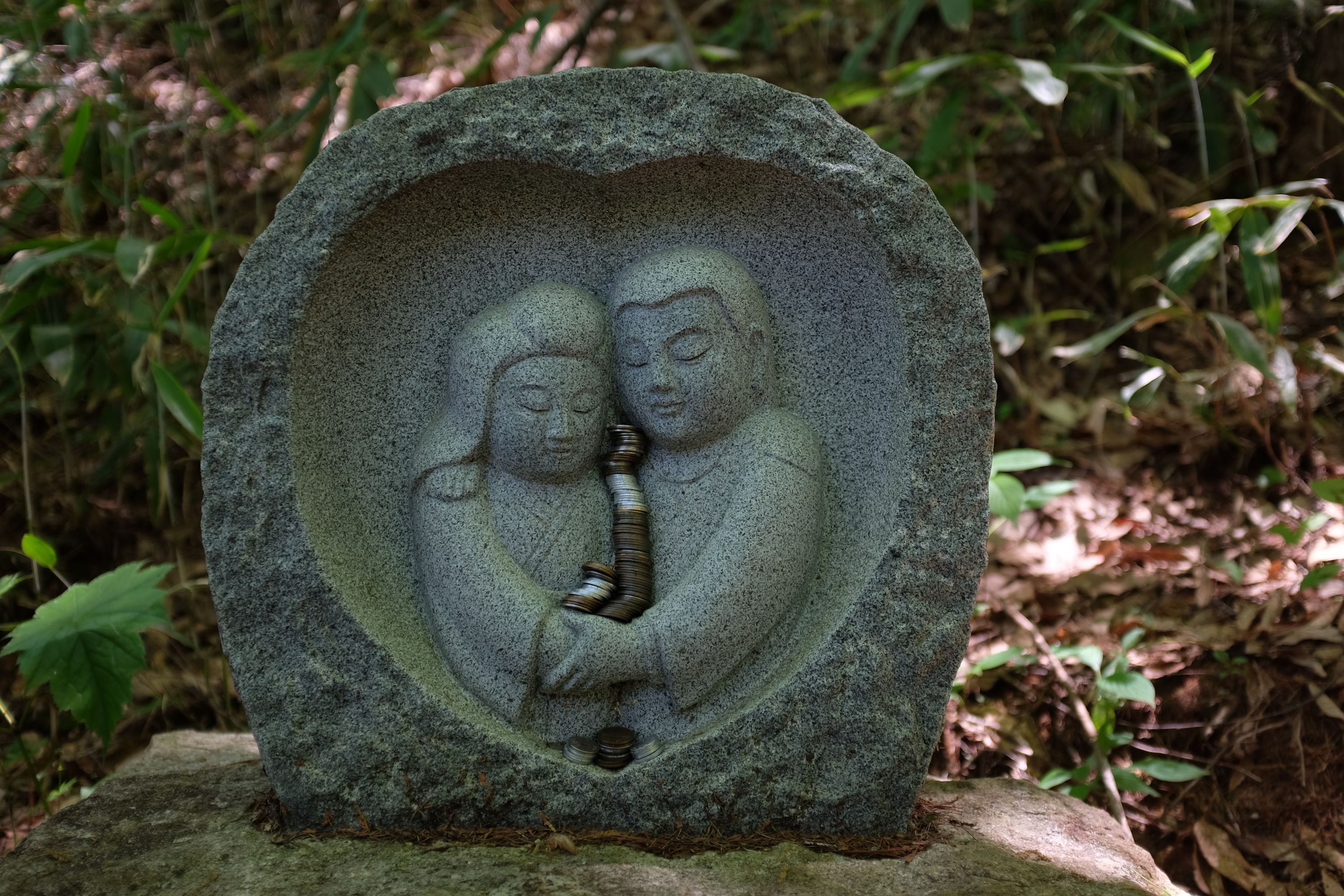 A small stone relief showing two human figures is adorned with stacks of coins.