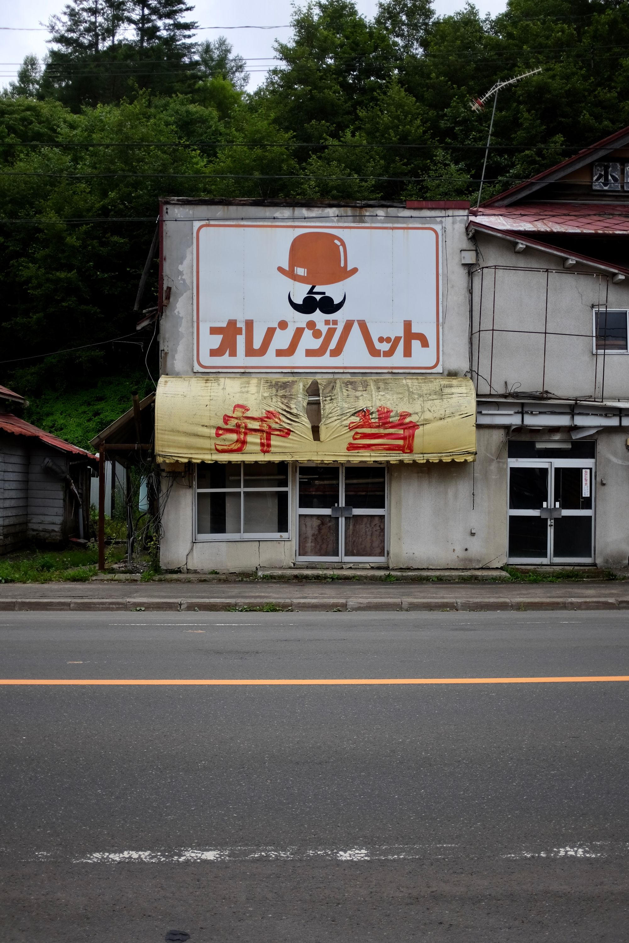 One of the many abandoned storefronts of Ochiai, this one showing the silhouette of a mustachioed man in an orange hat.