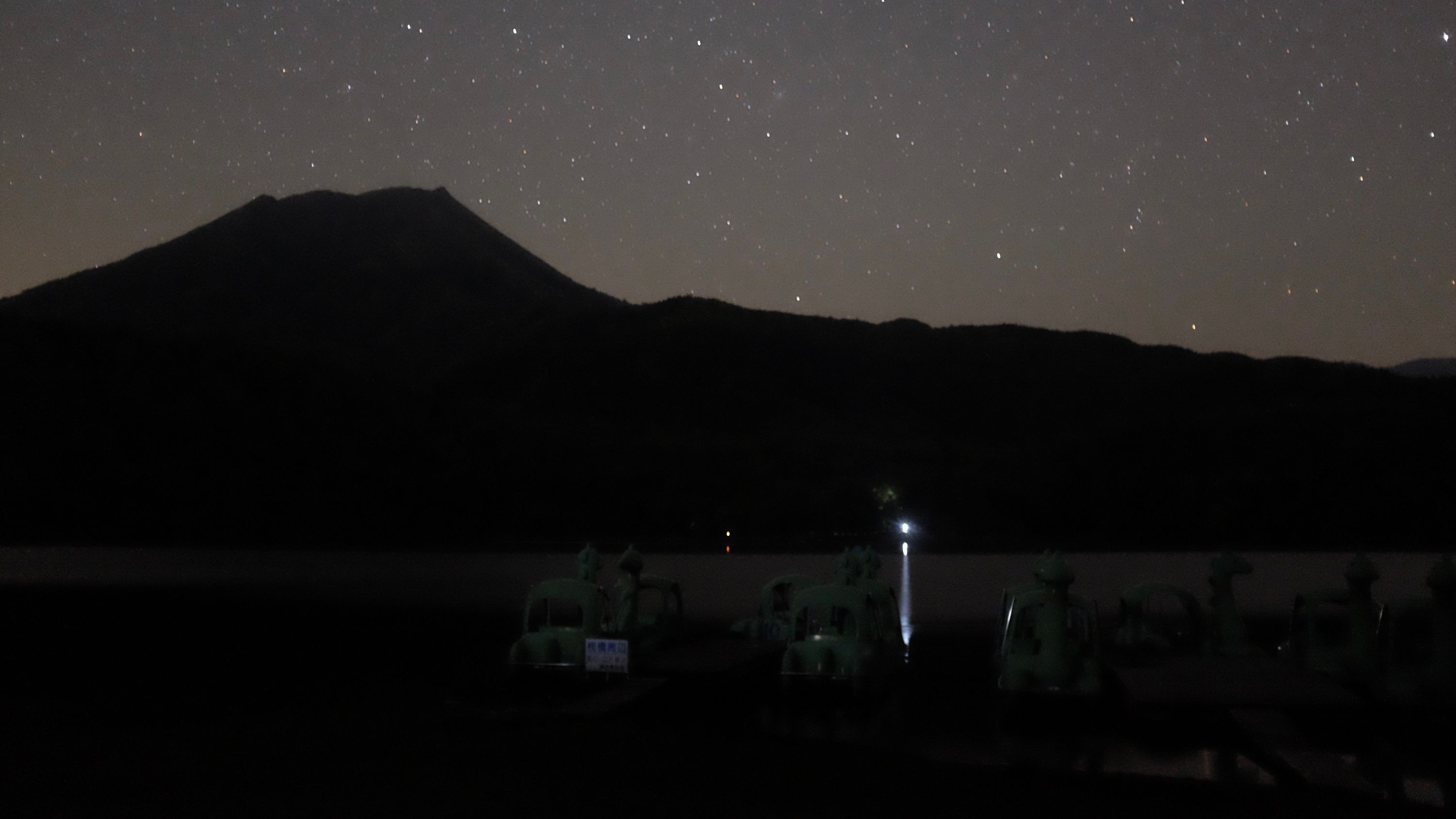 The silhouette of the volcano against a star-studded night sky, across a lake.