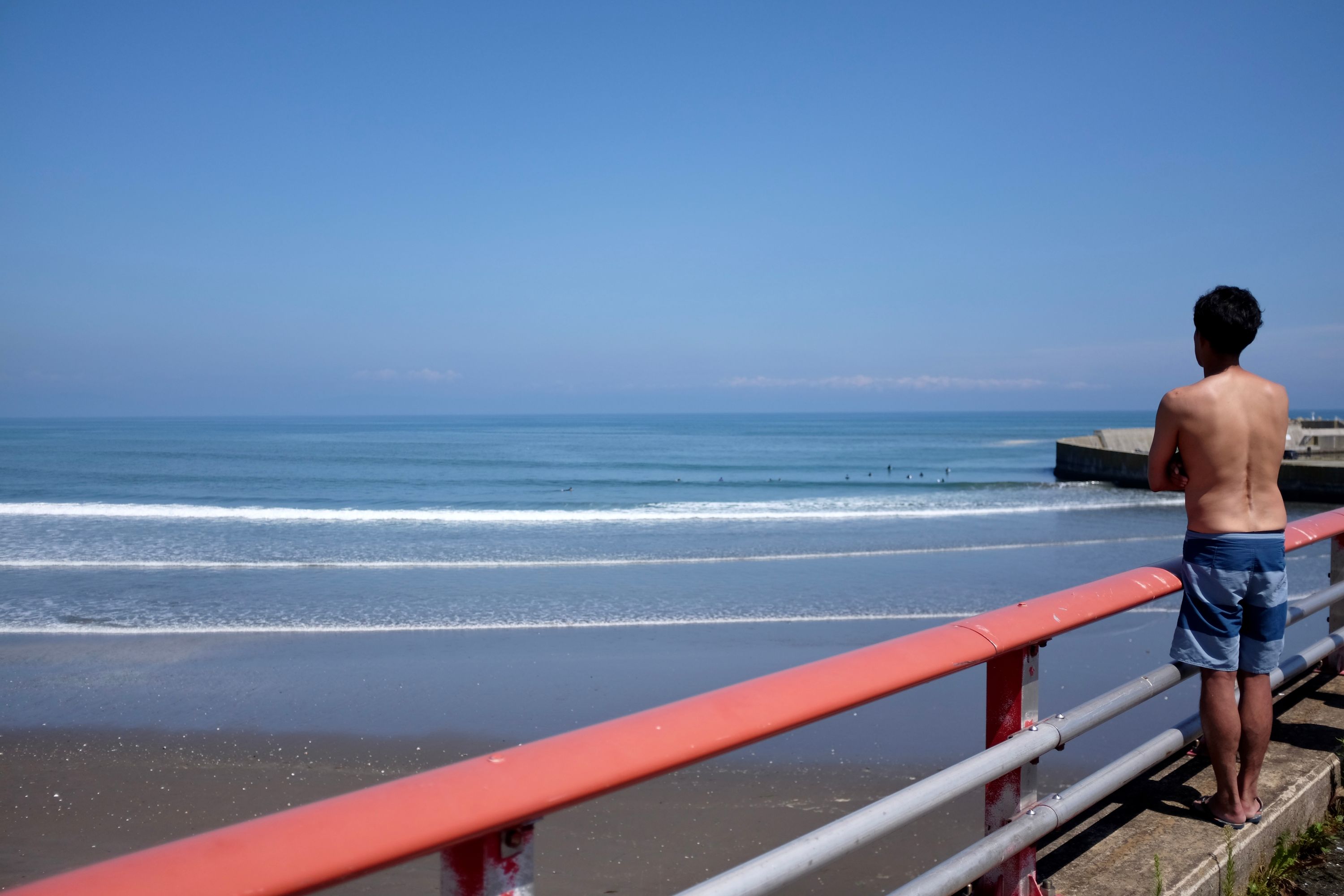 A man in board shorts watches the waves from a raised platform.