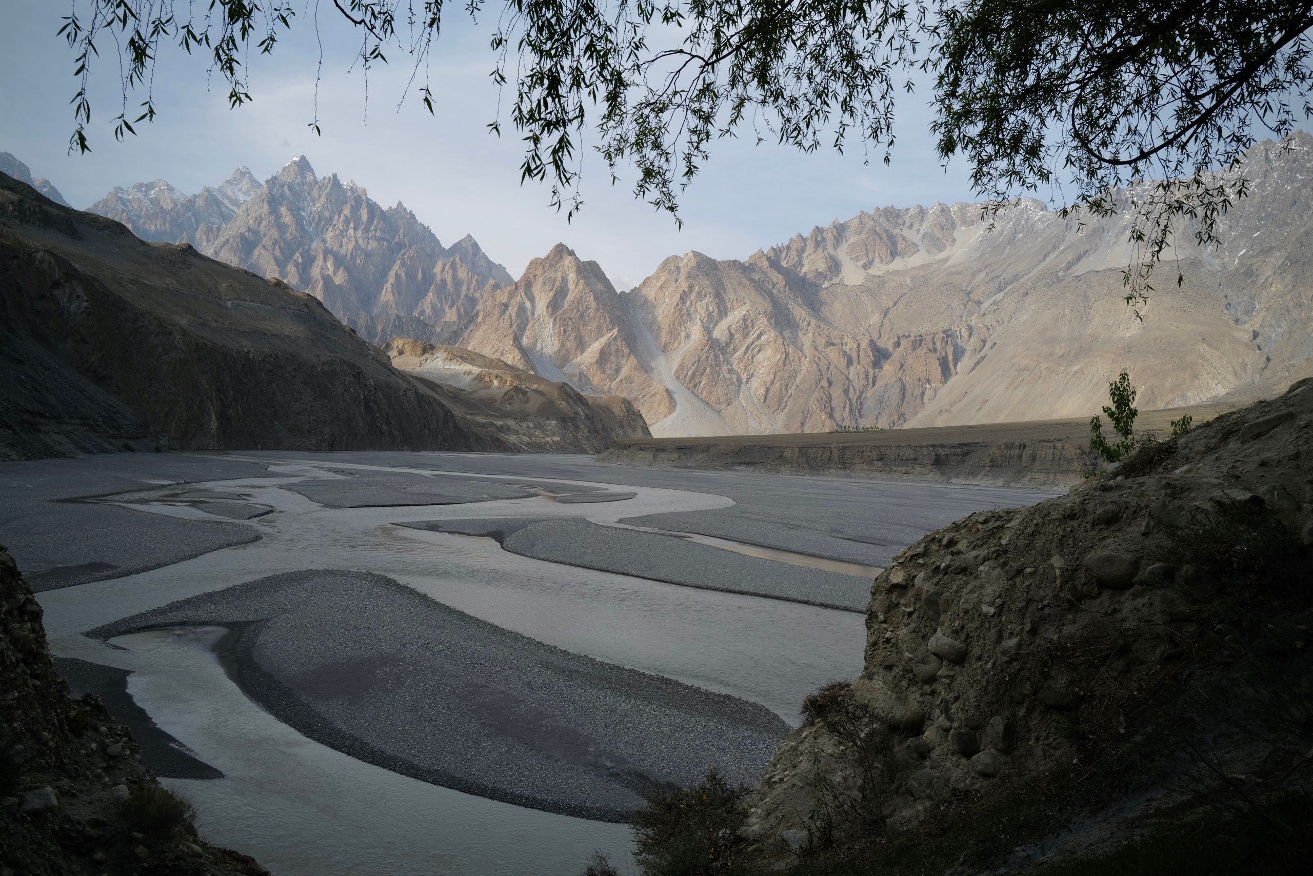 A wide, braided river flows in front of jagged mountain peaks.