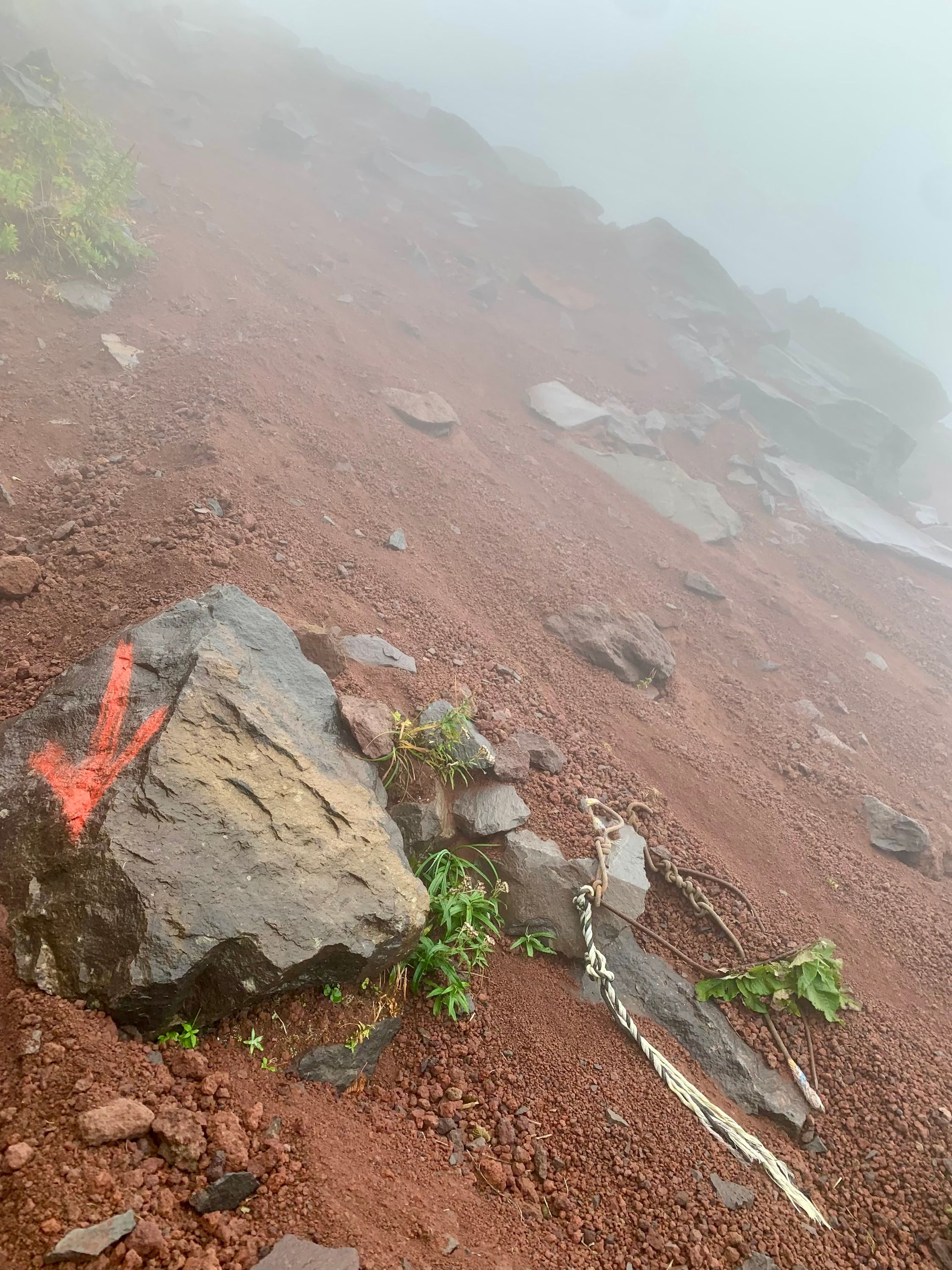 A torn rope lies on a slope of red volcanic scree and black rocks