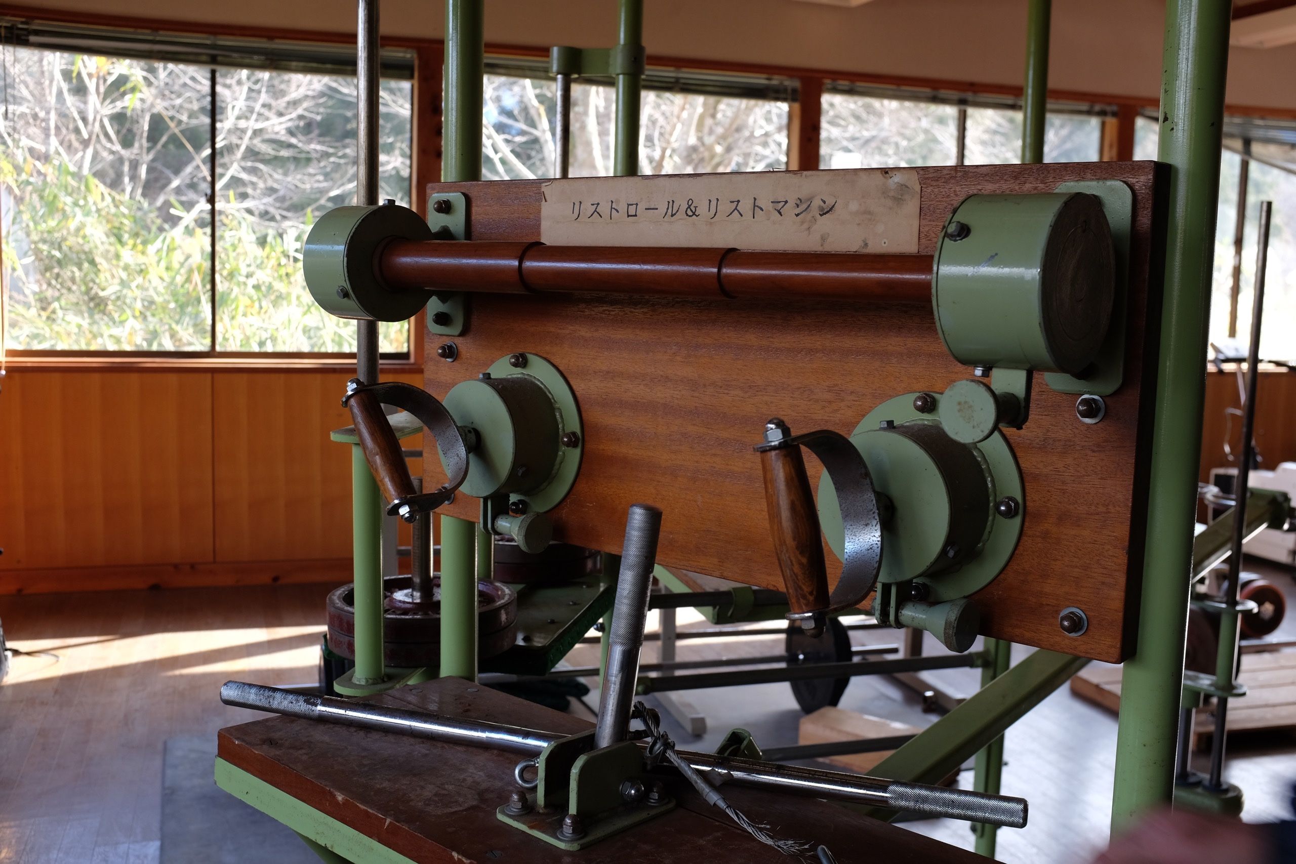 An old exercise machine, made of wood and green painted metal, in an old, sunlit room.