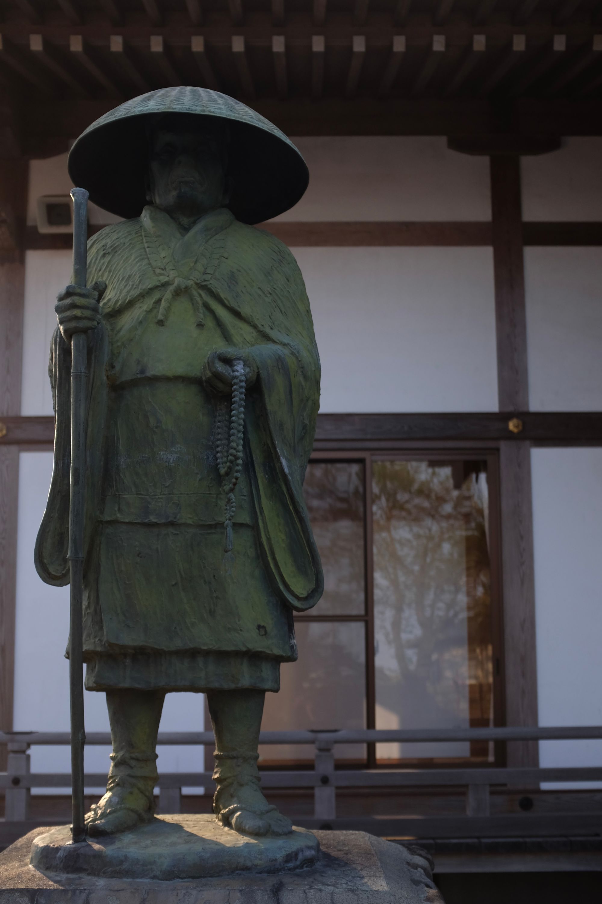A statue of the Buddhist monk Kōbō Daishi, dressed in sandals and a straw hat, carrying a tall walking stick.