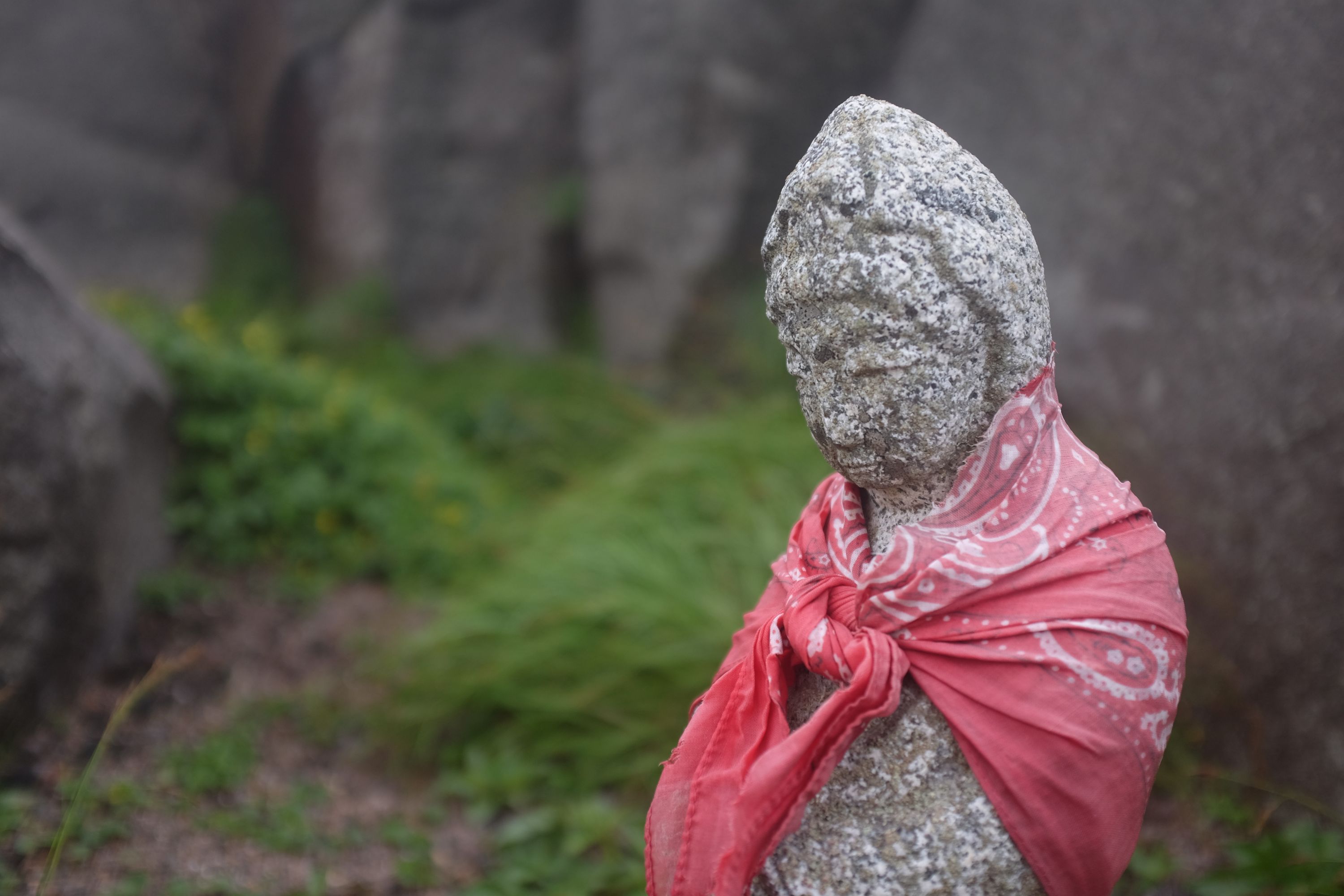 A small Buddhist statue with a red bandanna around its shoulders.