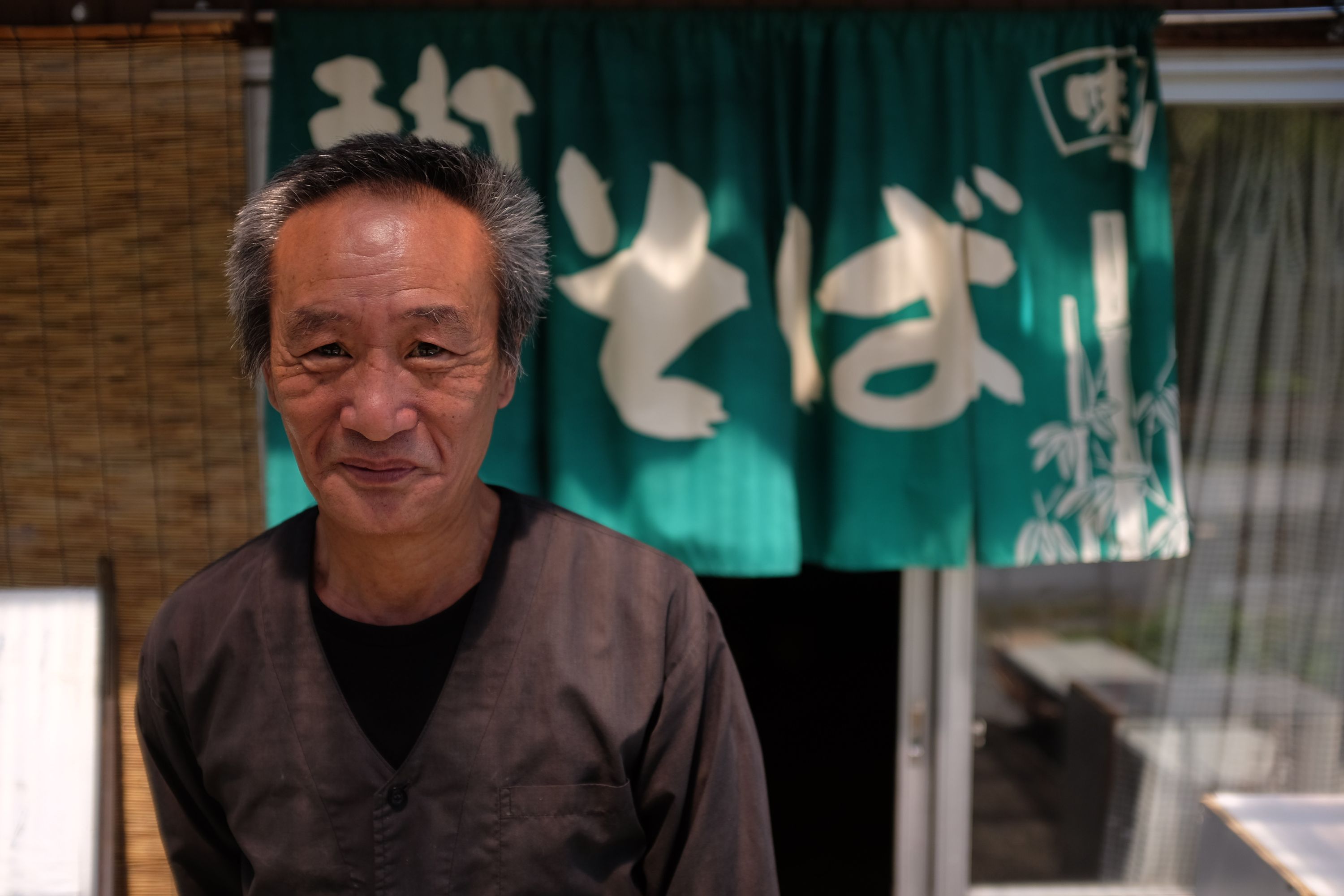 A Japanese man stands in front of his restaurant which sells buckwheat noodles.