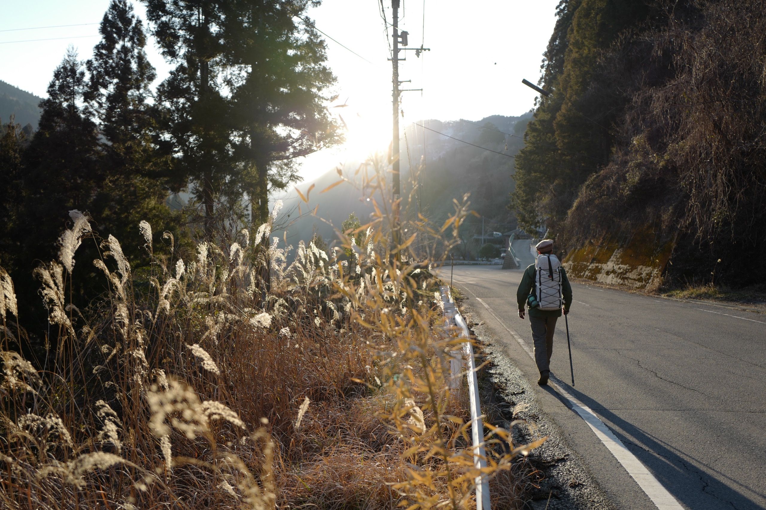 A man with a white rucksack, the author, walks down a country road.