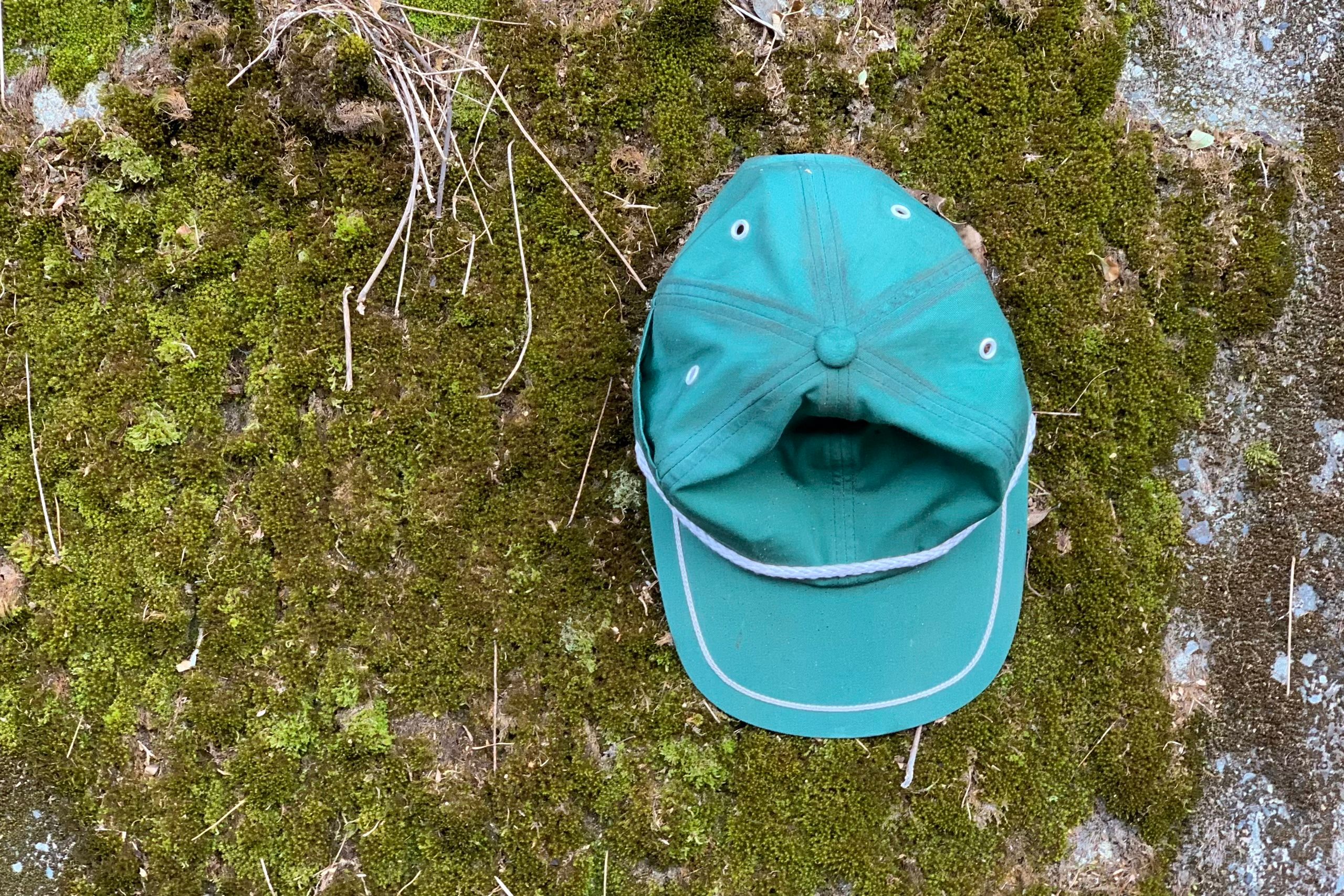 A green baseball cap hung on a wall covered with moss.