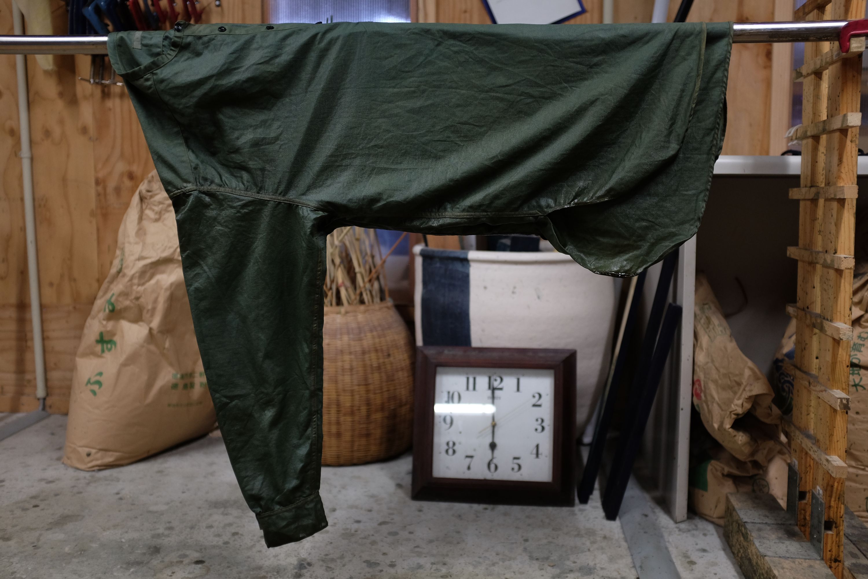 A freshly dyed jacket, bluish green in color, dries on a rail in a workshop.