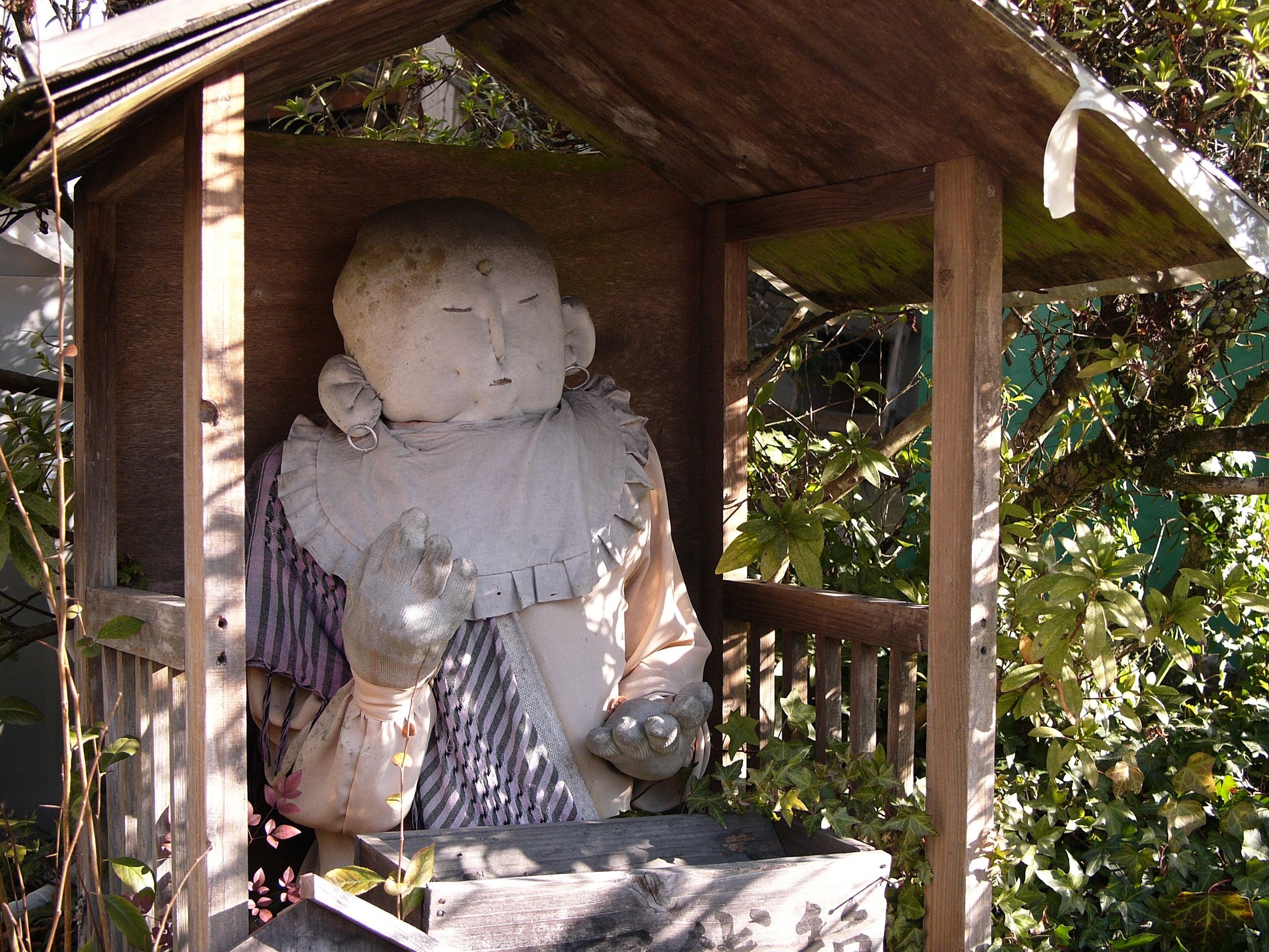 A fabric statue of a Buddha in a roadside shrine on a sunny morning.