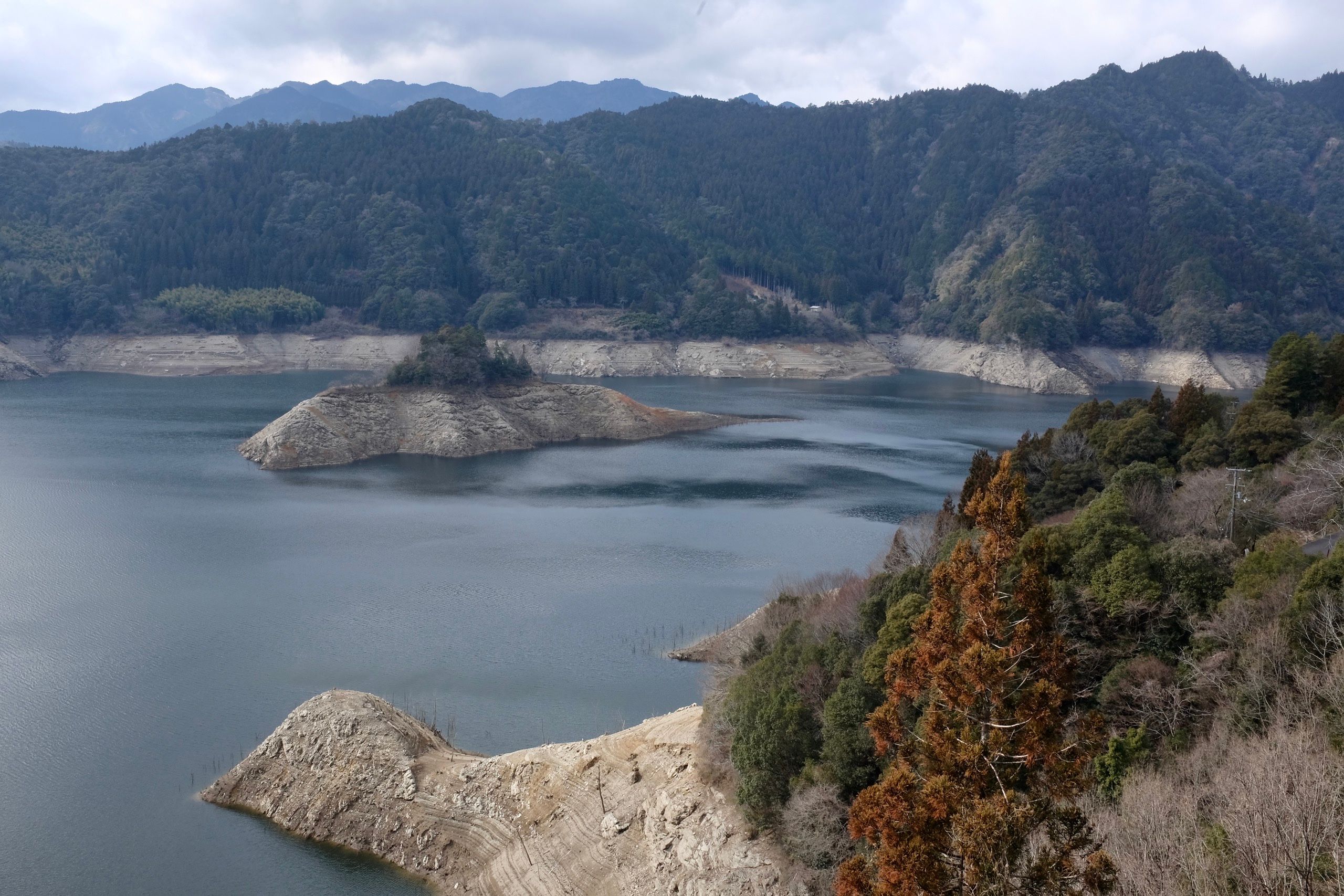 Panorama of an artificial lake with forested mountains behind it.