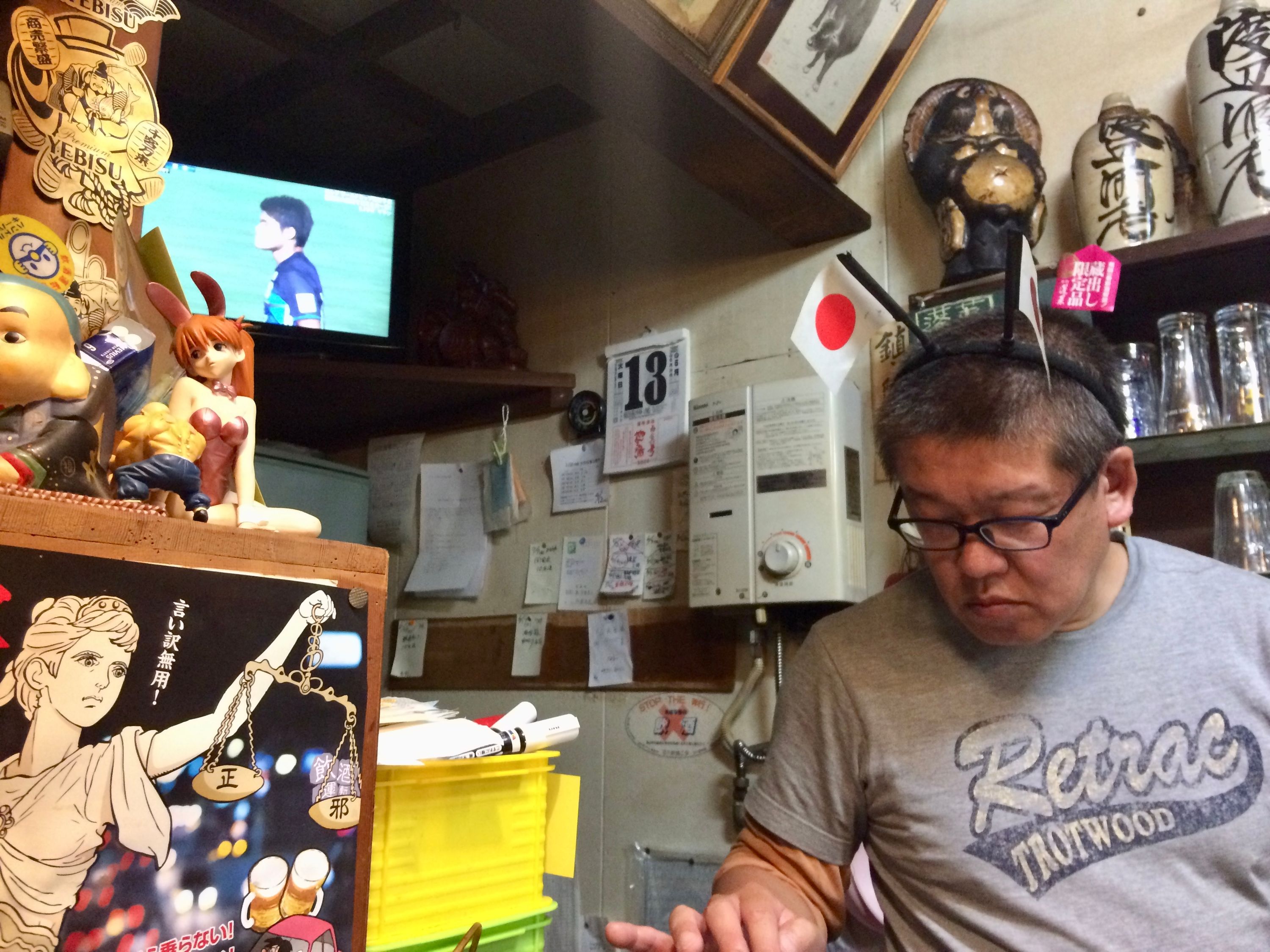 A bartender with two Japanese flags attached to his headband prepares food in a bar.