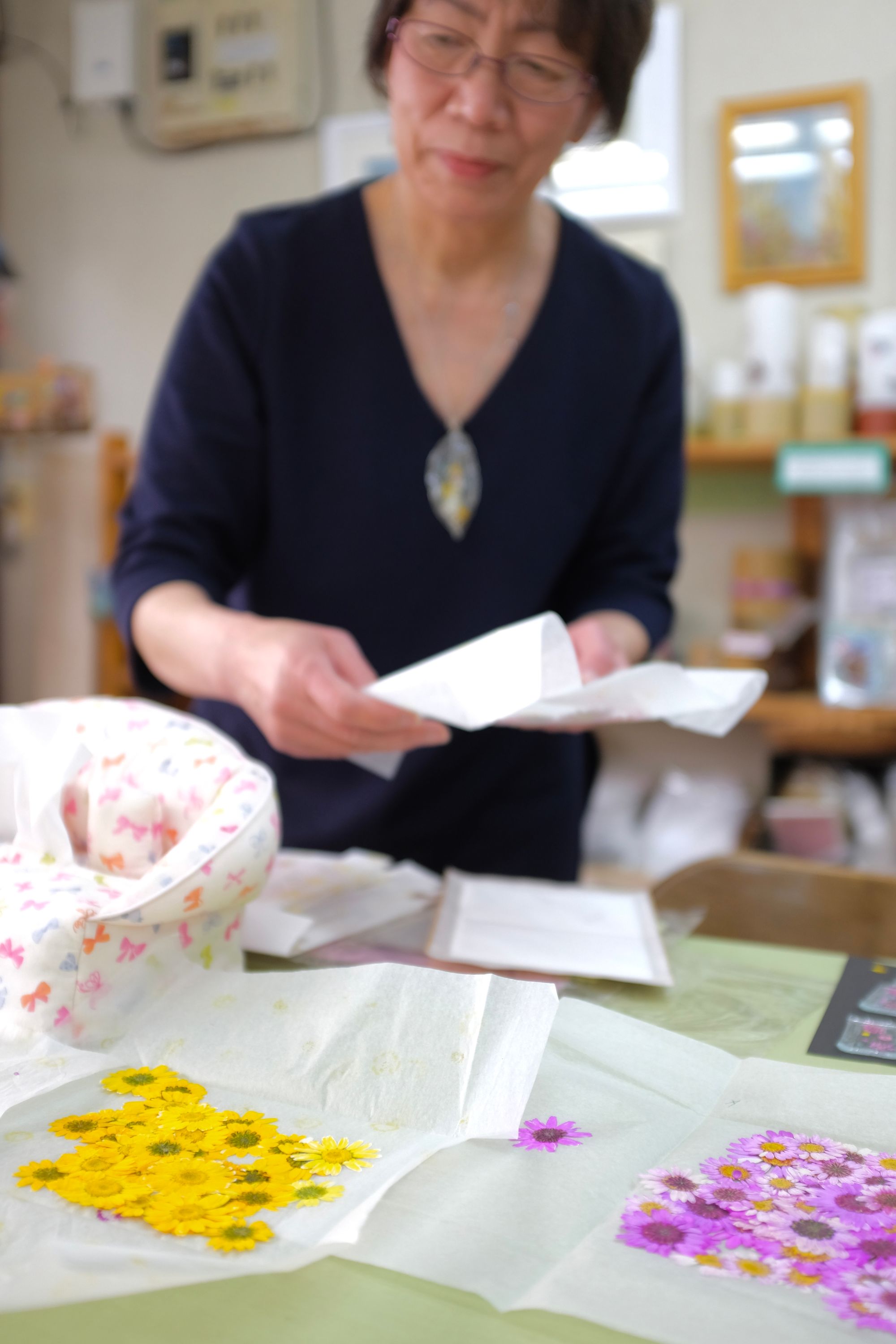 The woman stands behind a table, with her pressed flowers visible.