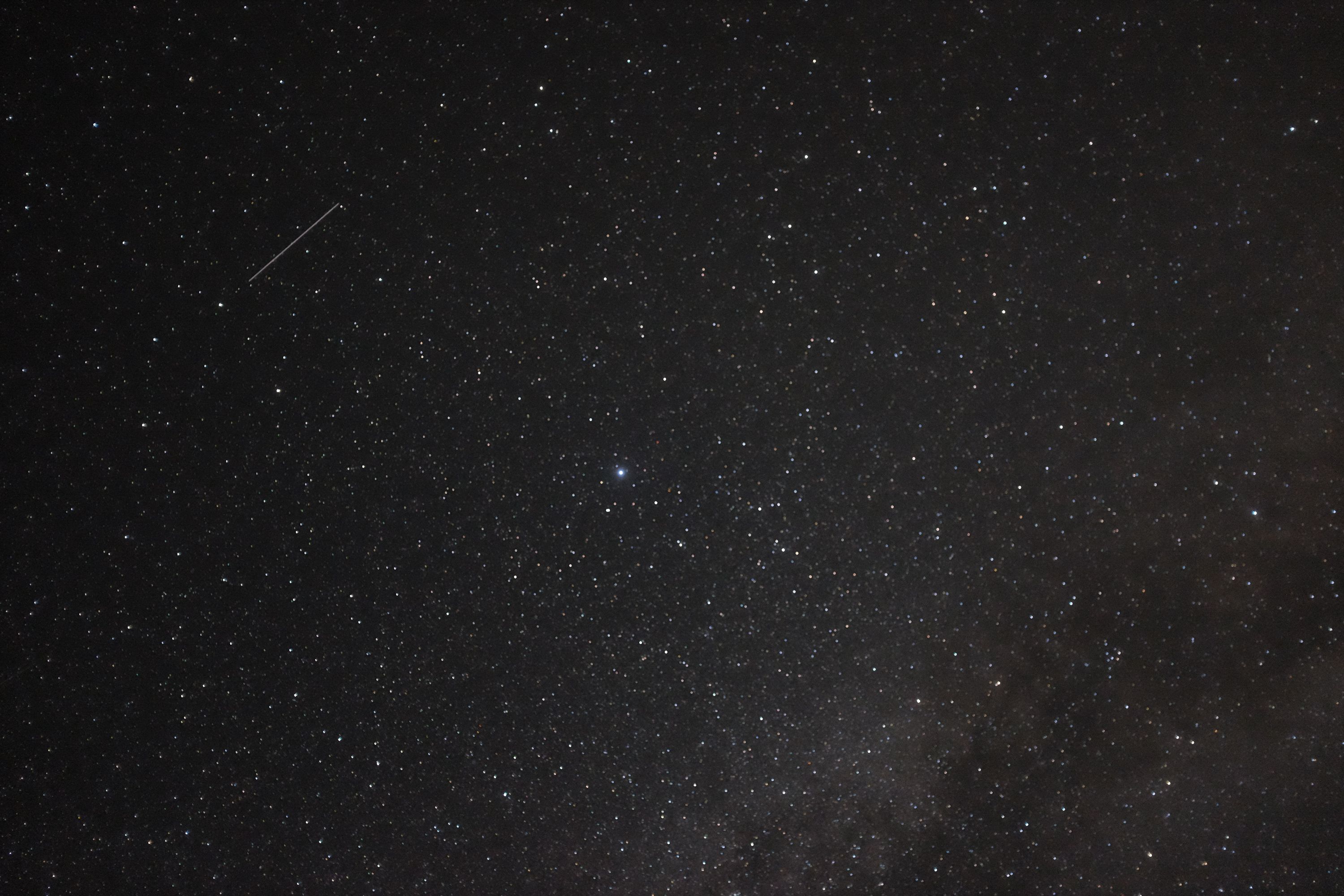 Looking up at the Milky Way across the night sky, with a plane passing through the stars.