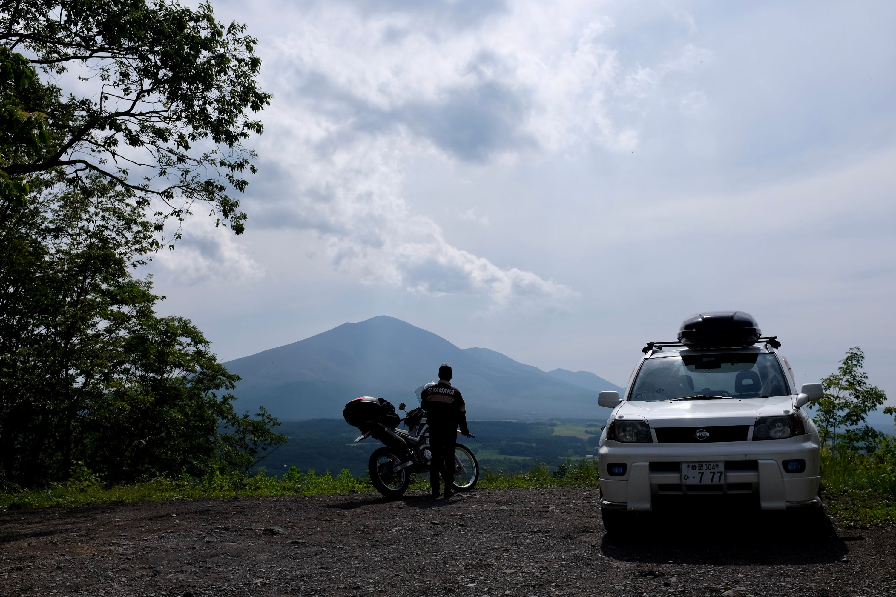A man stands by his motorcycle and watches a big volcano, Mount Asama.