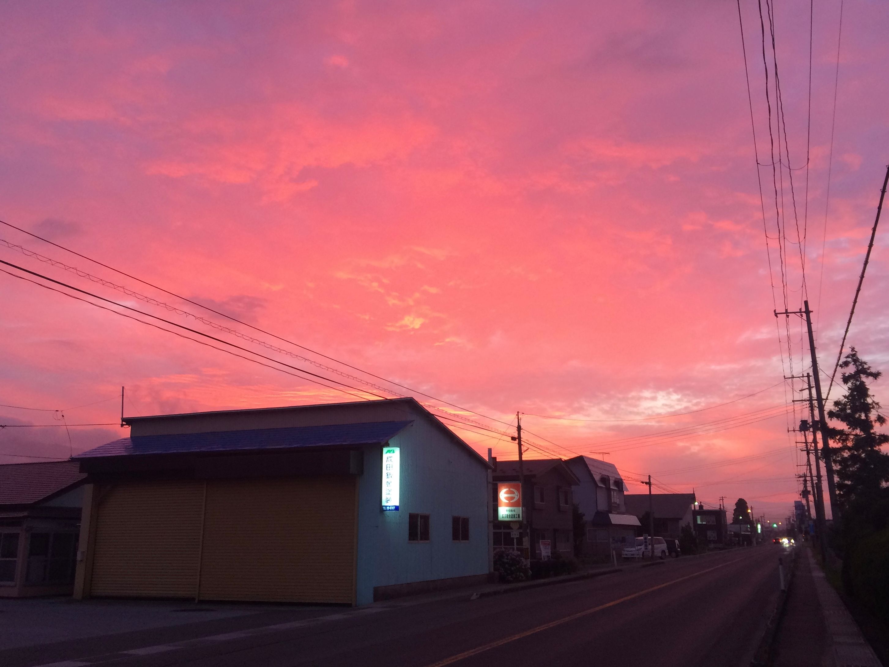 A radiant pink-orange sunset above a street.