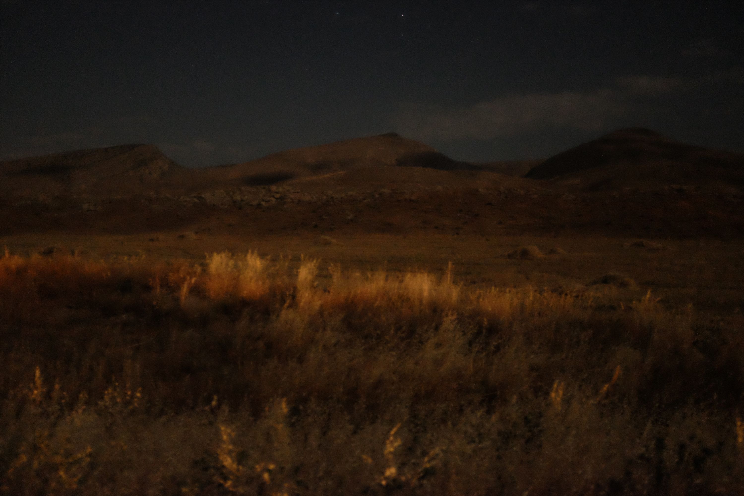 Fields glow with strange golden light in front of a line of low hills.