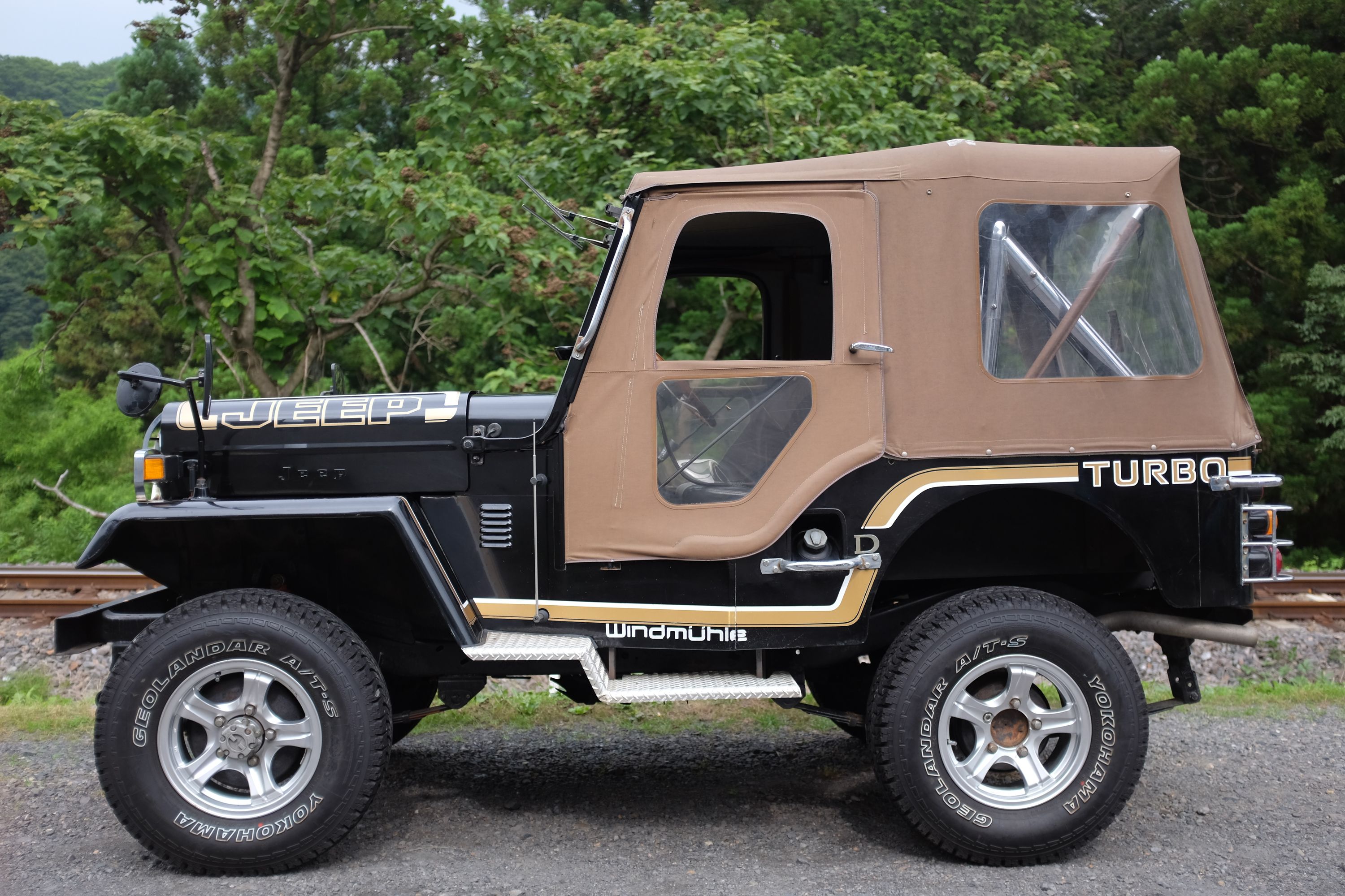 A black and tan Jeep by the railroad tracks.