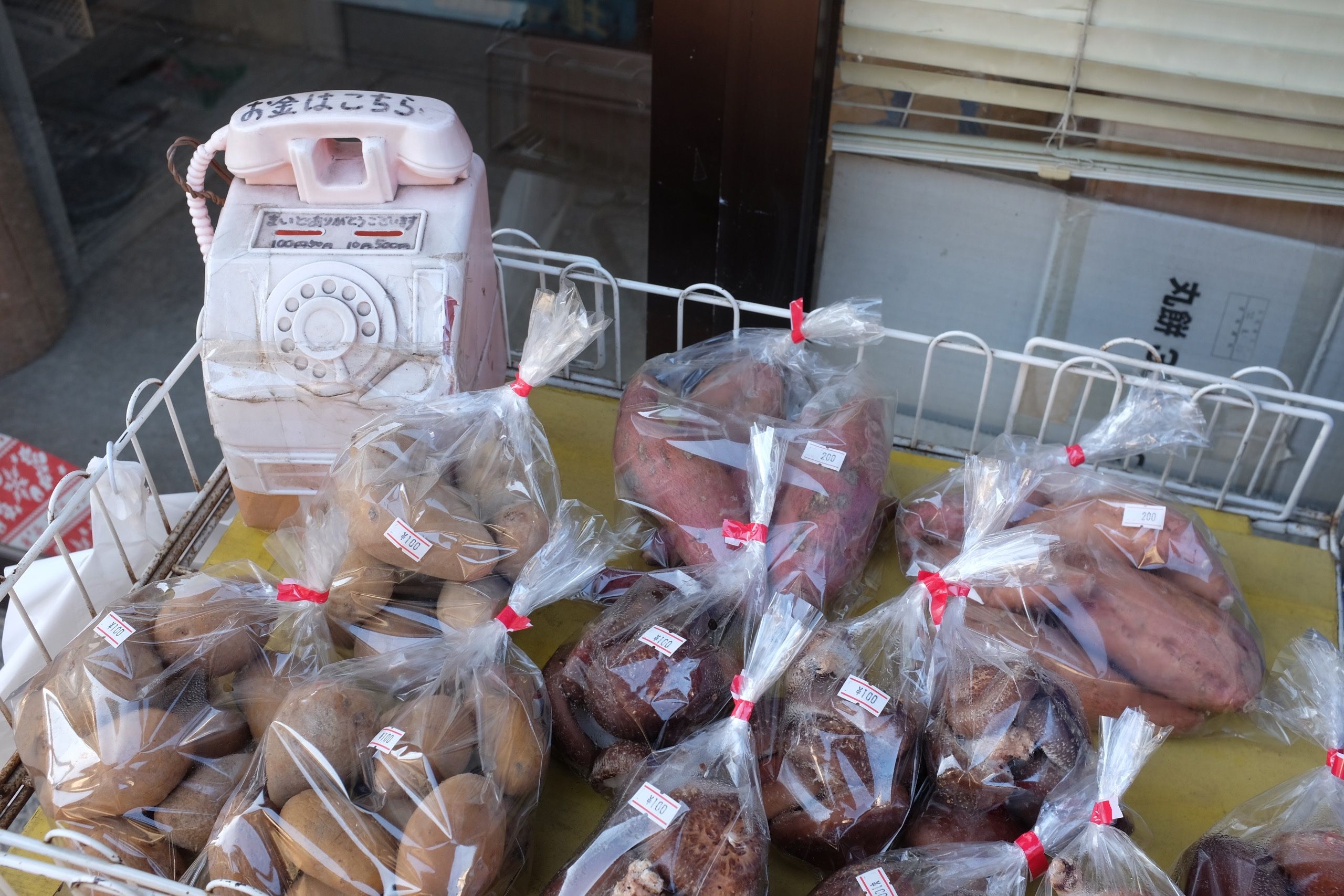 Plastic bags of sweet potatoes for sale with a hollow plastic telephone to drop the money into.