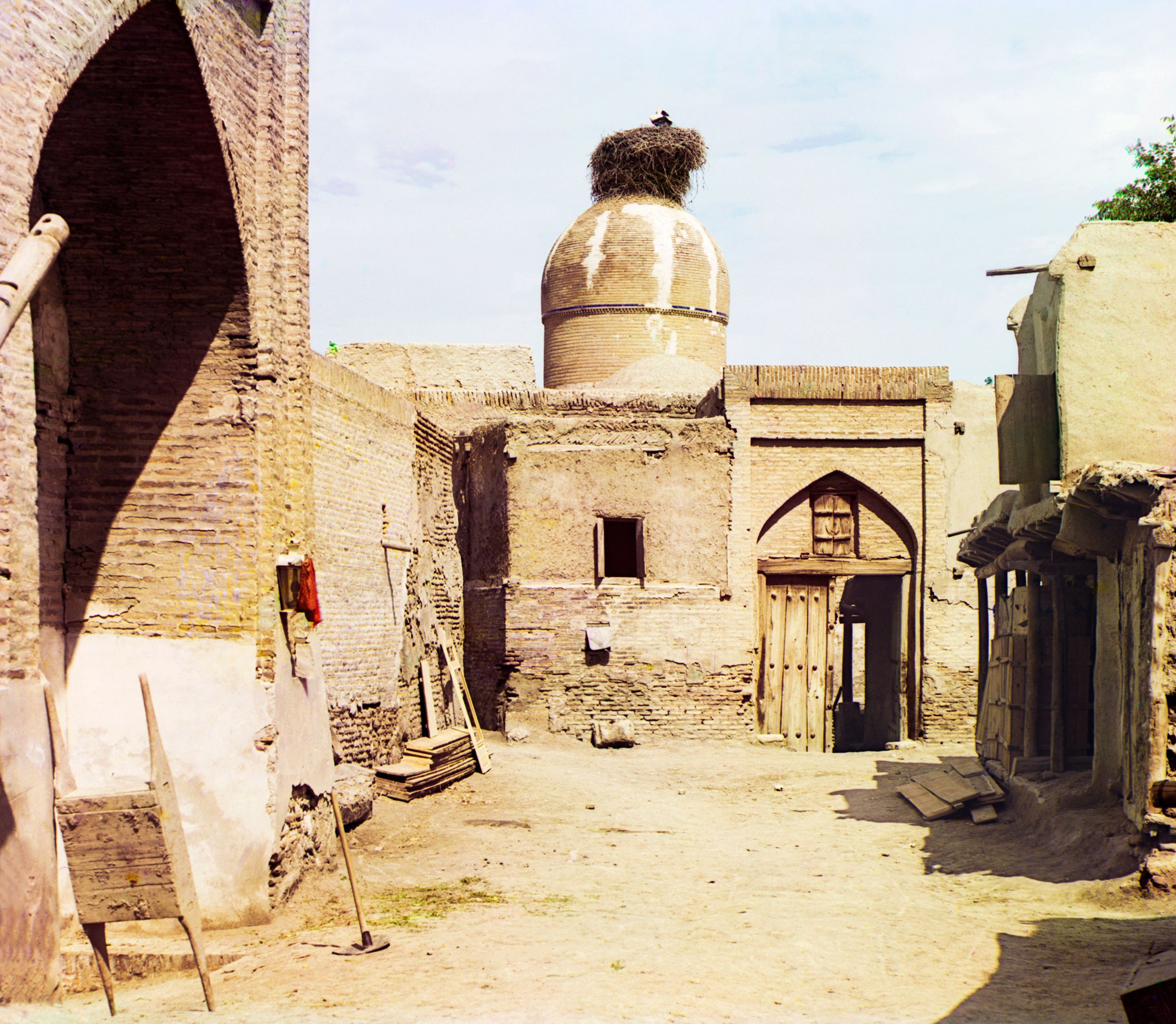 View of a courtyard, adobe buildings, and a bird’s nest atop a dome