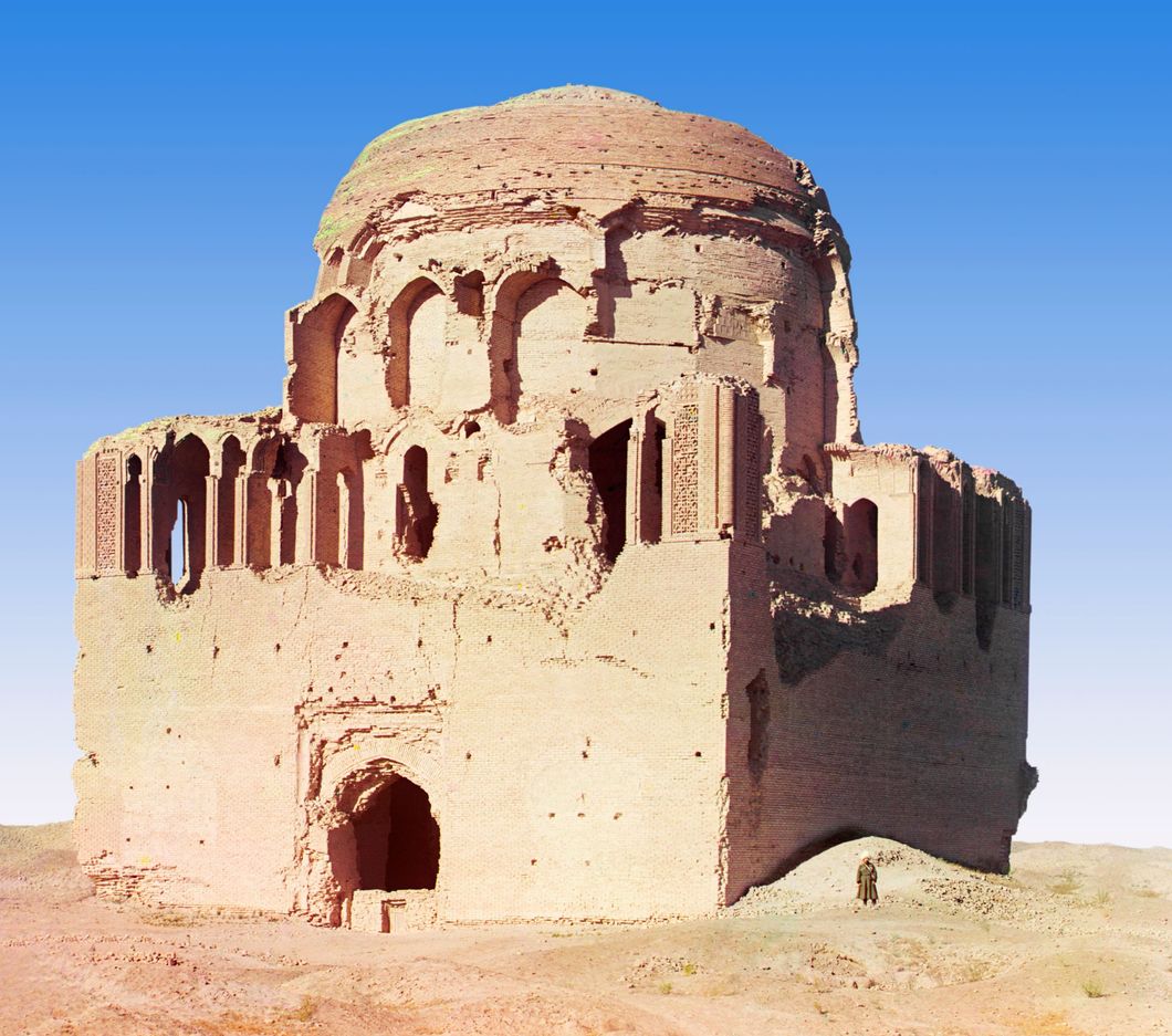 Front view of a crumbling mosque, with a man standing beside it