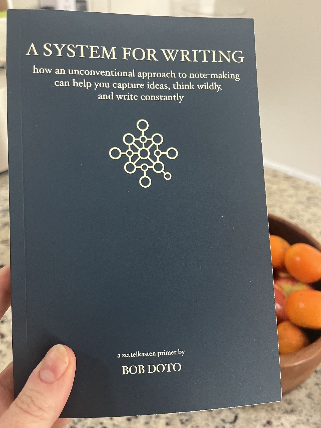 Book held in hand: A System for Writing by Bob Doto. The book cover is dark blue