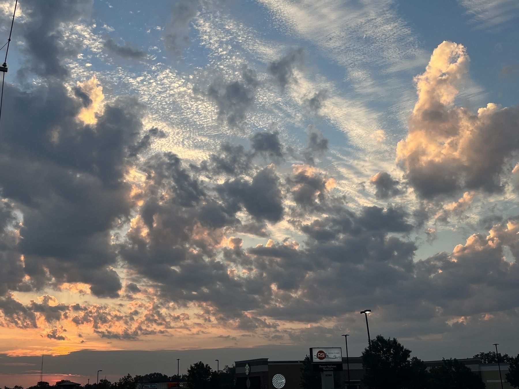Orange sunrise glow in bottom left and lots of gray and white clouds on a blue sky