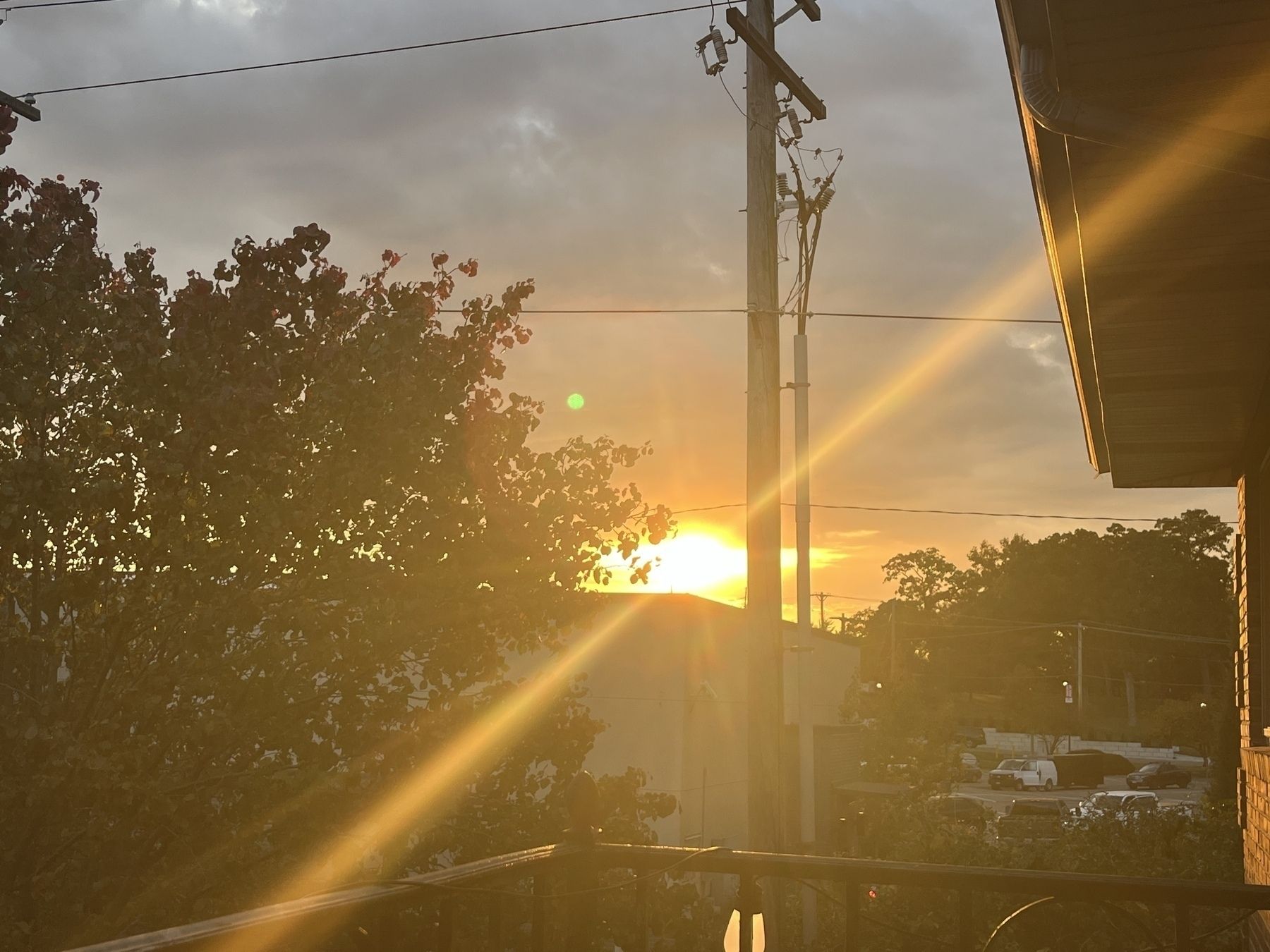 A sunset with light beaming out over a flat cafe roof with power lines, a parking lot, and the edge of a brick building in view