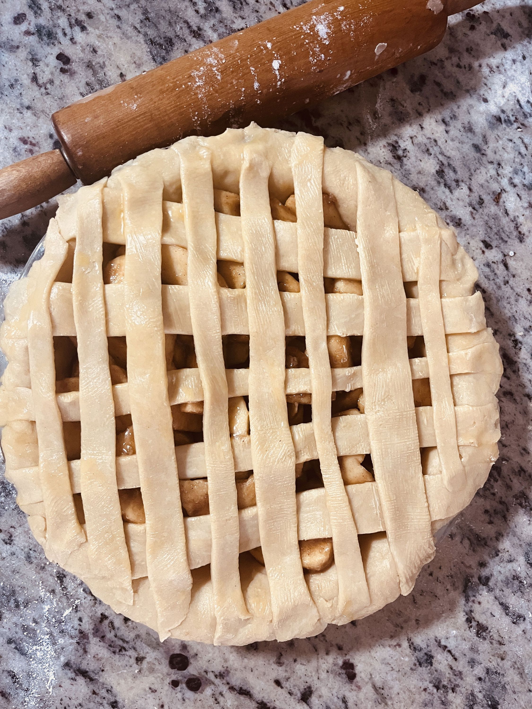 An unbaked apple pie with lattice crust sitting beside a rolling pin