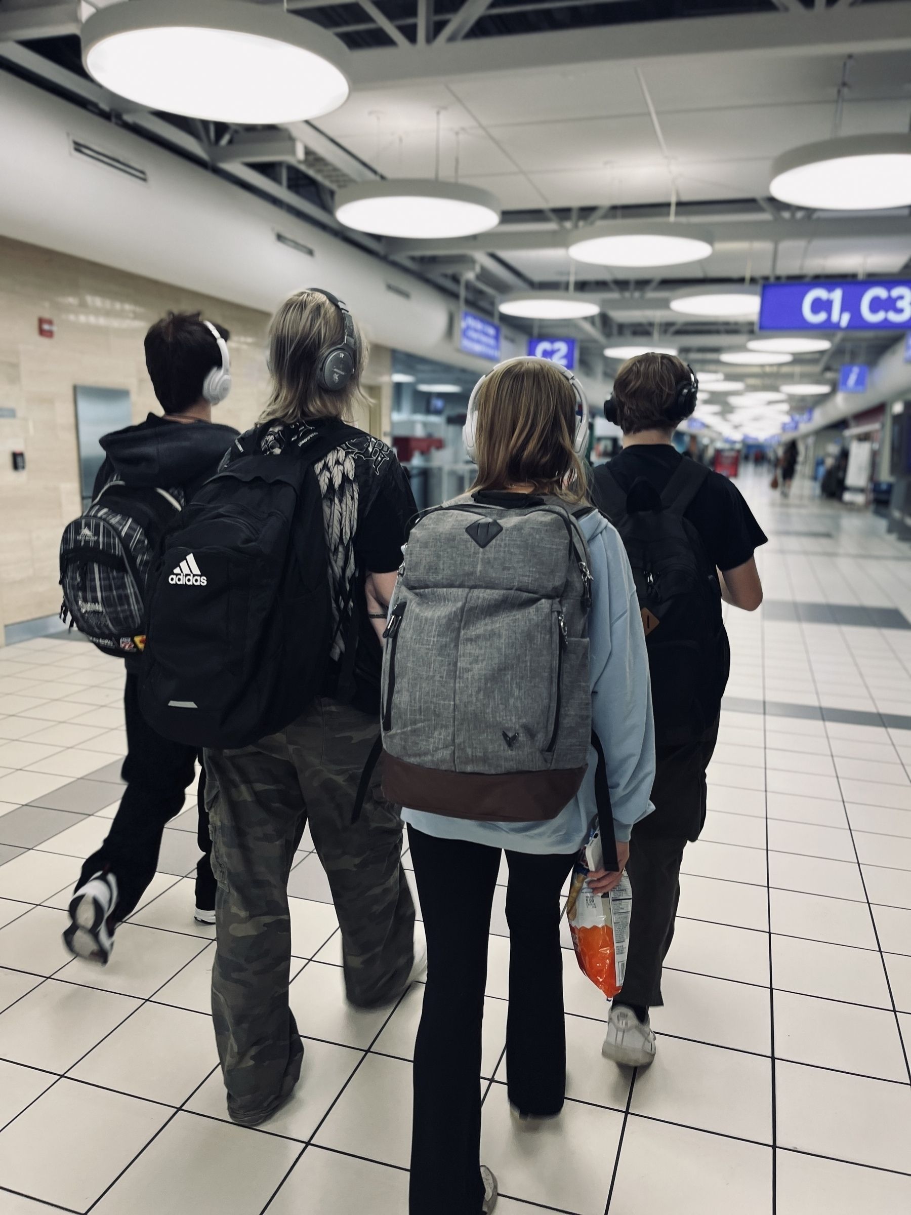 Four teenagers seen from behind walking thru an airport wearing backpacks