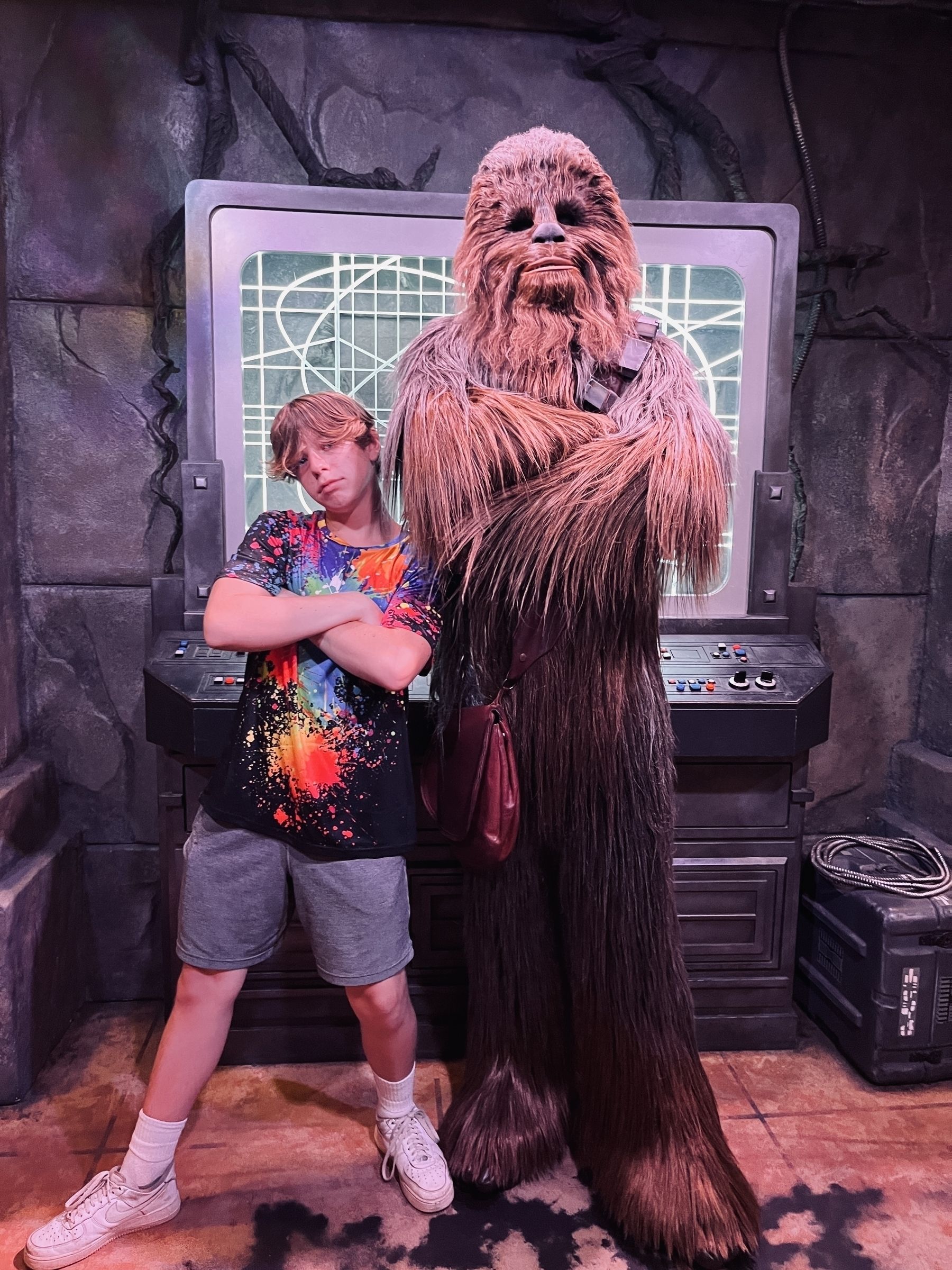 A boy in a bright shirt standing next to Chewbacca Wookiee